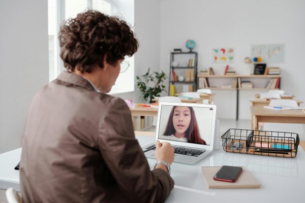 A teacher engages in an online class from an empty classroom, using a laptop for learning.