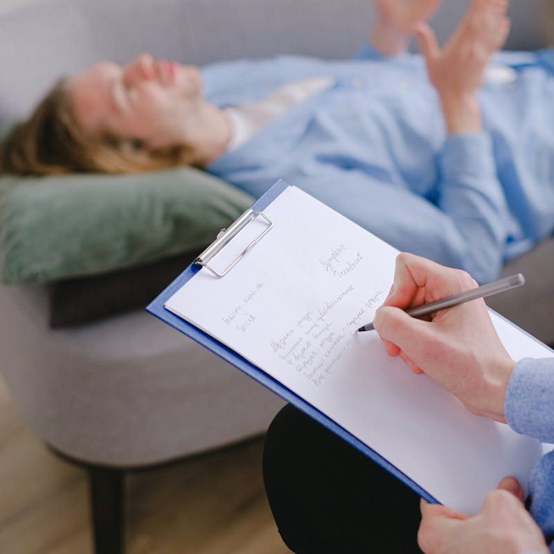 Therapist taking notes while a patient lies on the couch during a therapy session.